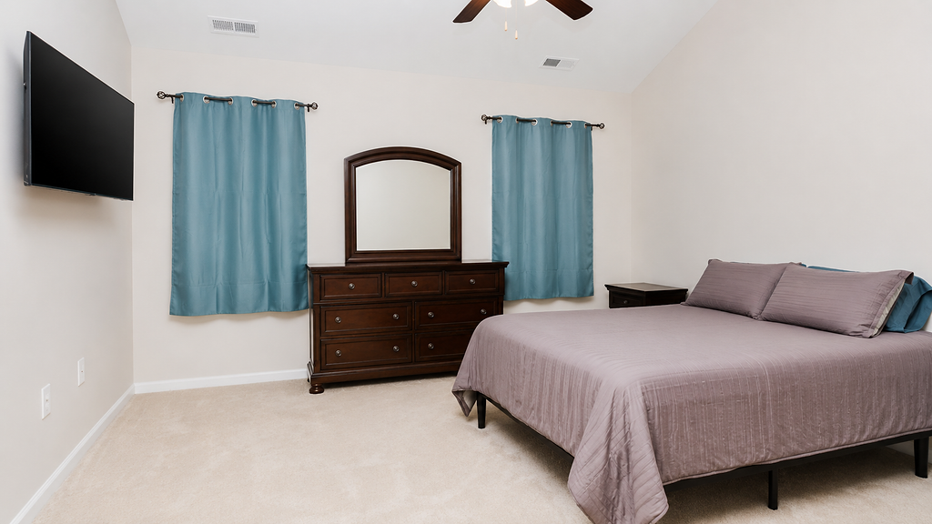 Primary bedroom with tall ceilings, mounted television and soft natural light