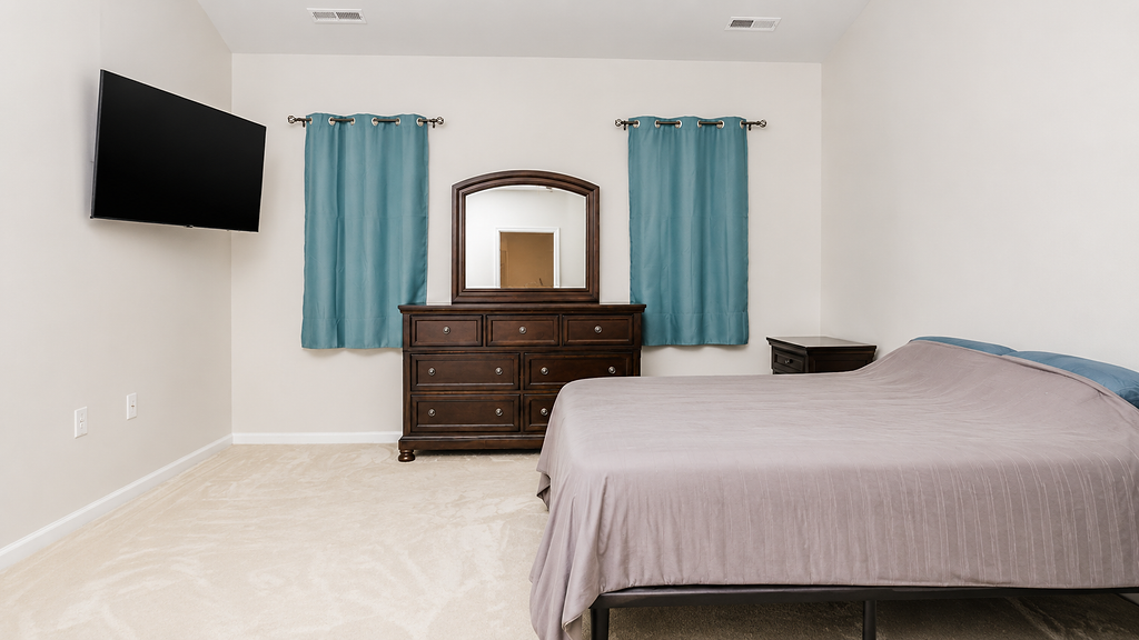 Spacious bedroom with dresser, mounted television and blue curtains